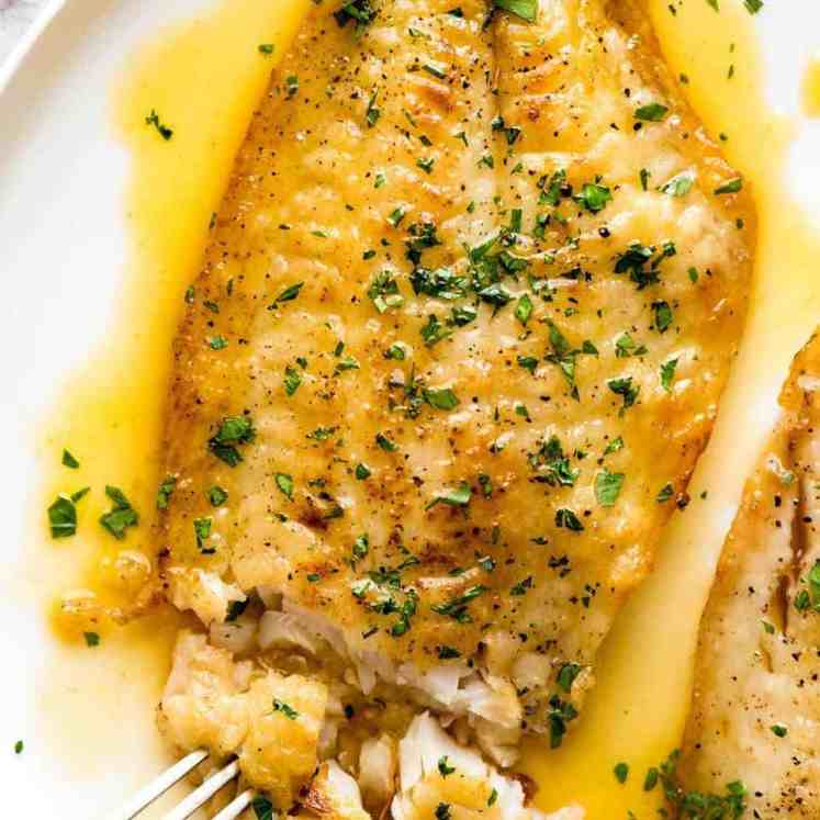 Overhead photo of a crispy pan fried fish fillet drizzled with Lemon Butter Sauce and sprinkled with parsley. On a white plate.