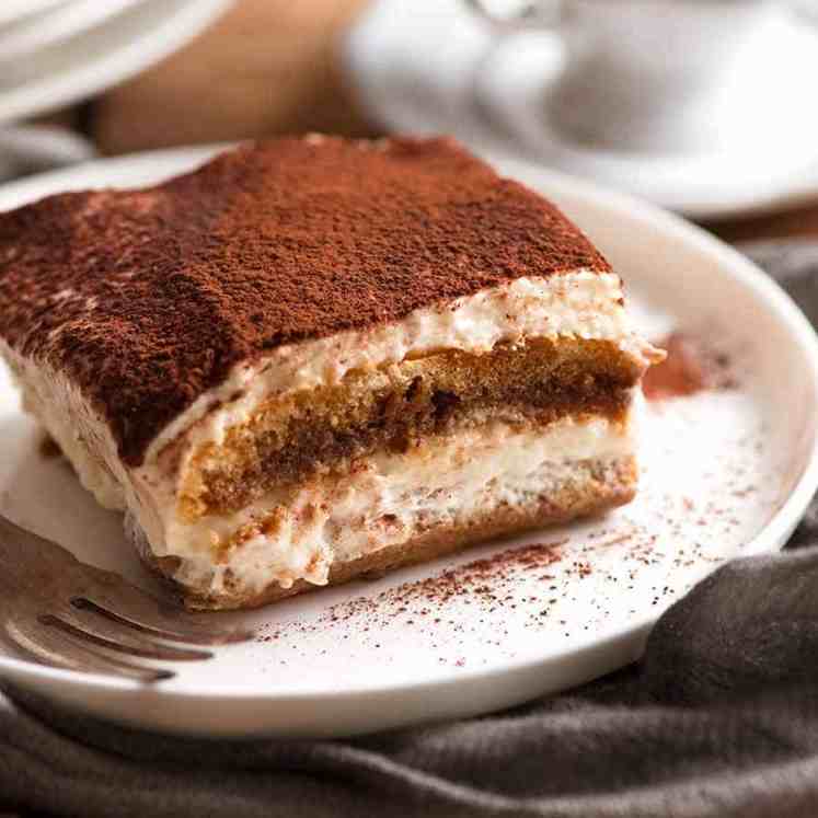 Close up of a slice of Tiramisu on a white plate, ready to be eaten